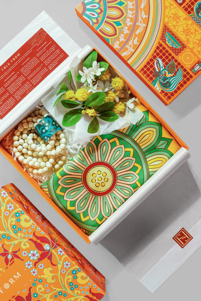 Open orange Folk Form gift box with a folded silk scarf in white tissue, flowers and beads