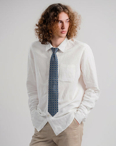 Model wearing a dark blue patterned silk tie, 3.1 inch wide, with a white linen shirt