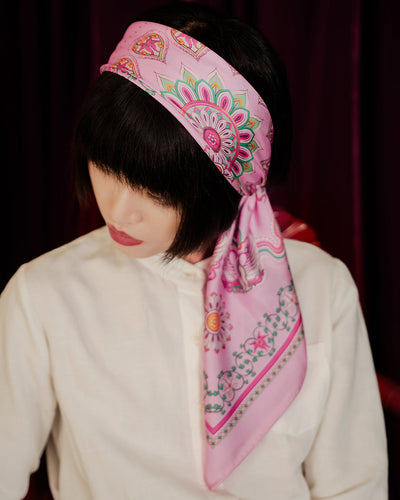 Woman wearing a pink Phoenix Dance silk scarf folded into a headband over a white shirt