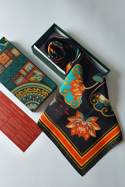 Black lotus silk scarf spilling from an open green Folk Form gift box beside the printed lid and a red care card