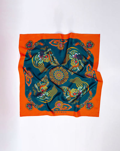 Orange and dark green Dragon Dreams silk scarf laid flat on a pale surface