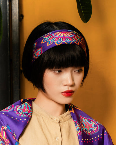 Purple Phoenix Dance silk scarf worn as a headband with a camel shirt against a mustard wall