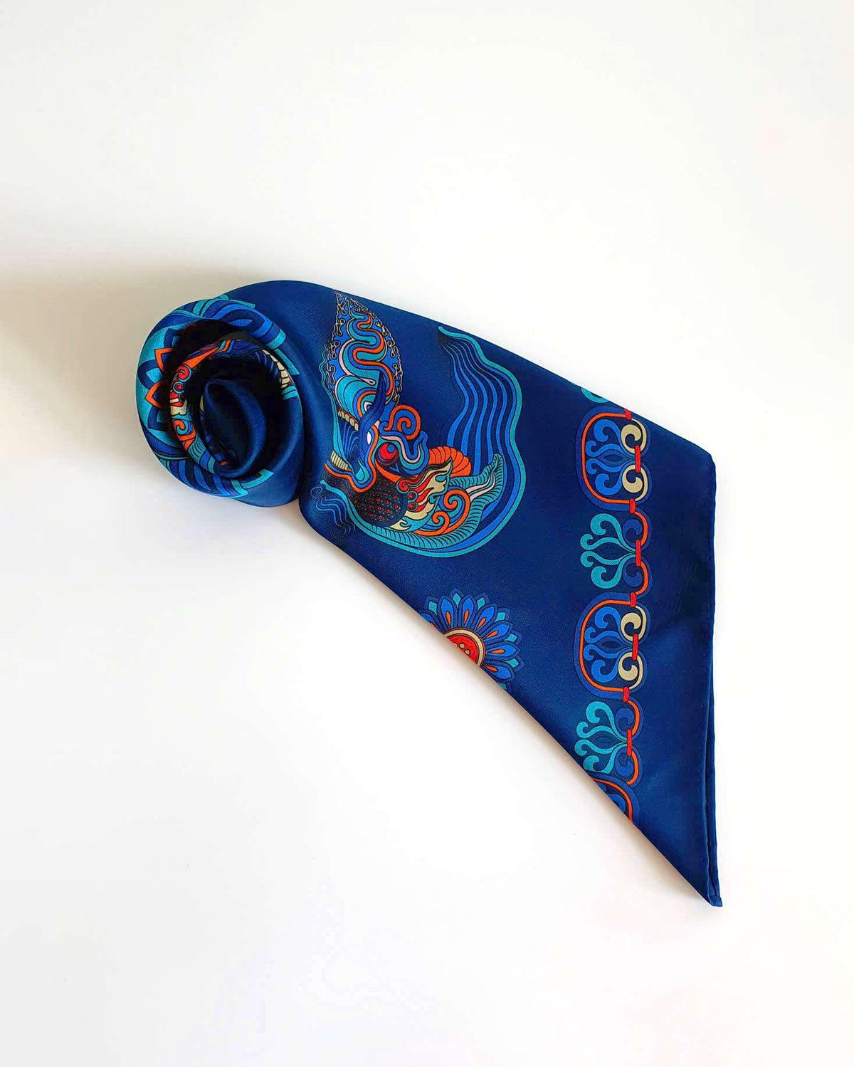 Navy blue silk scarf rolled into a rosette, showing the dragon print and hand-rolled hem