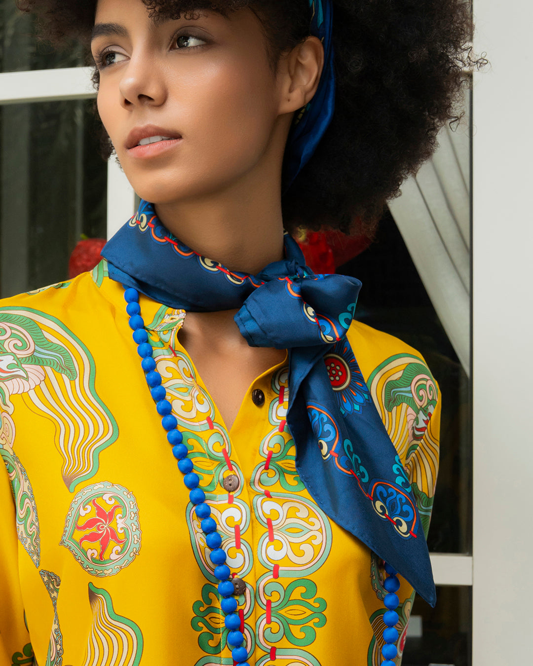 Navy Dragon of Grace silk scarf knotted loosely at the neck over a yellow shirt