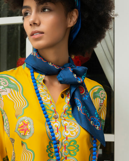 Navy Dragon of Grace silk scarf knotted loosely at the neck over a yellow shirt