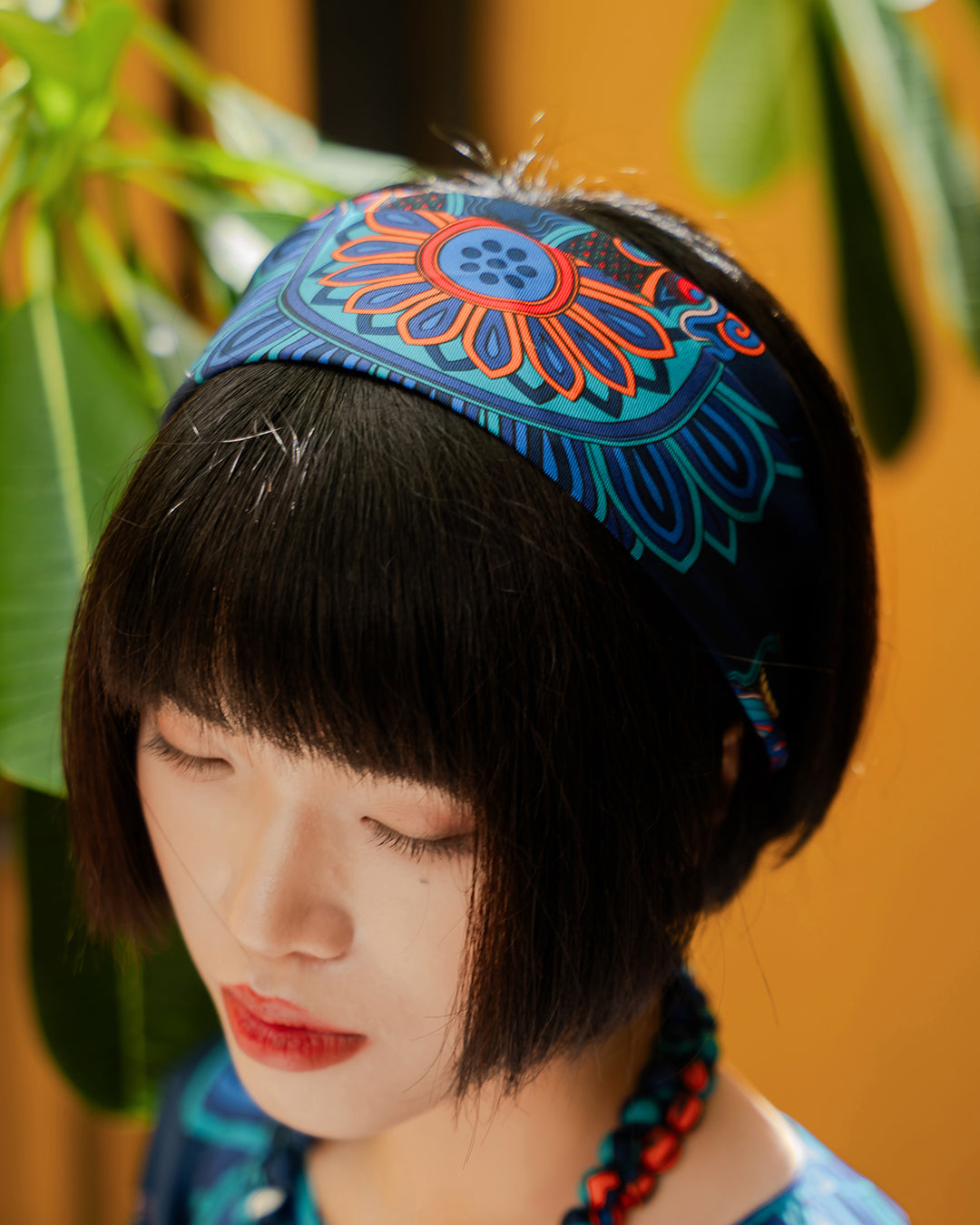Navy silk scarf folded as a wide headband with a sunburst medallion