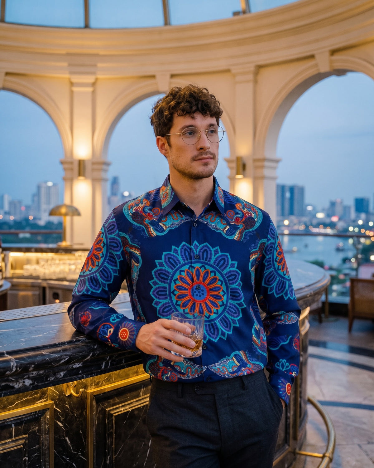 Man in a navy silk shirt with hand-printed Dragon of Grace at a marble rooftop bar at blue hour