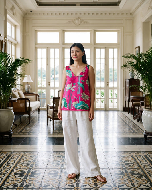 Woman wearing a hot pink silk tank top with hand-printed Imperial Lotus and white wide-leg trousers in a cream French neoclassical hotel living room